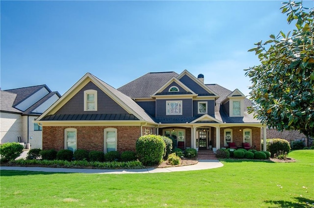 craftsman-style home featuring covered porch, brick siding, a chimney, and a front lawn