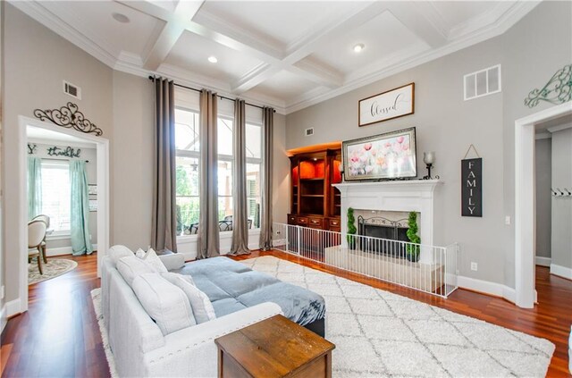 living room featuring visible vents, ornamental molding, wood finished floors, beamed ceiling, and a fireplace with raised hearth