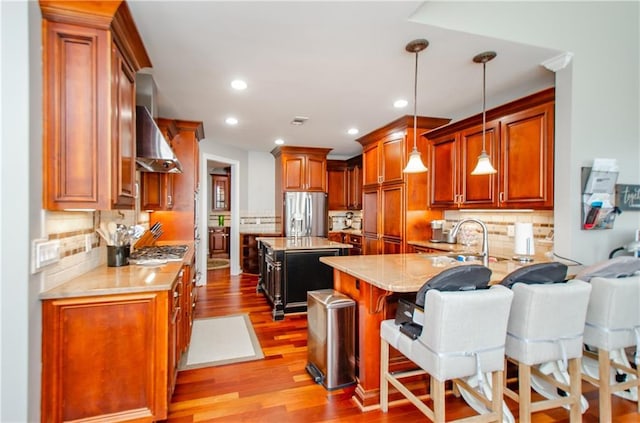 kitchen with backsplash, appliances with stainless steel finishes, wood finished floors, a sink, and wall chimney exhaust hood