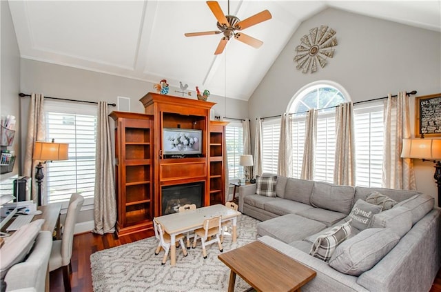 living area with ceiling fan, a glass covered fireplace, wood finished floors, and high vaulted ceiling