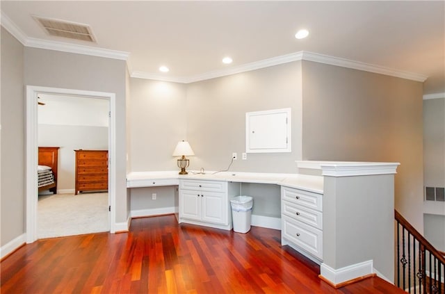 unfurnished office with crown molding, dark wood-type flooring, built in desk, and visible vents