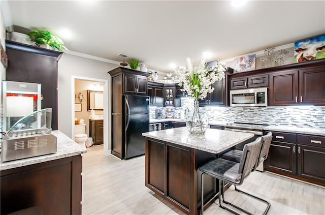 kitchen with ornamental molding, a center island, light wood-style flooring, appliances with stainless steel finishes, and backsplash