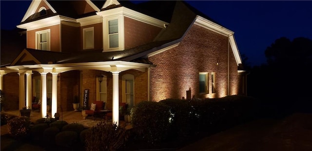 back of house at night featuring brick siding and covered porch