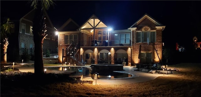 back of house at twilight with stairs, a patio area, a pool with connected hot tub, and a balcony