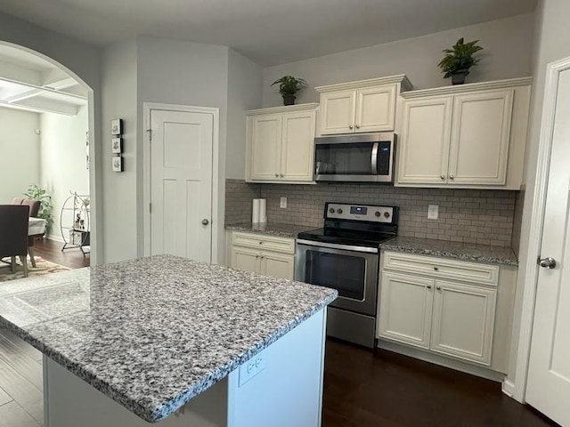 kitchen featuring light stone countertops, stainless steel appliances, dark hardwood / wood-style flooring, backsplash, and a kitchen island