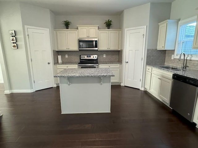 kitchen featuring light stone countertops, appliances with stainless steel finishes, tasteful backsplash, sink, and a center island