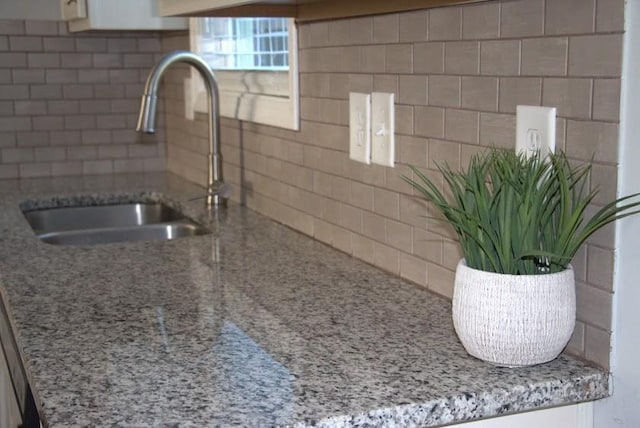 details featuring backsplash, light stone countertops, and sink