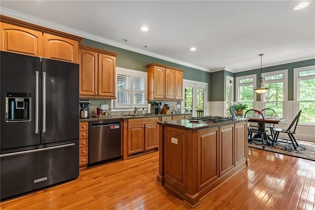 kitchen featuring pendant lighting, a kitchen island, stainless steel appliances, light wood-type flooring, and crown molding