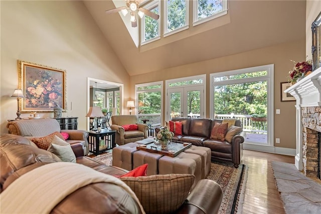 living room featuring ceiling fan, a stone fireplace, high vaulted ceiling, hardwood / wood-style flooring, and a healthy amount of sunlight