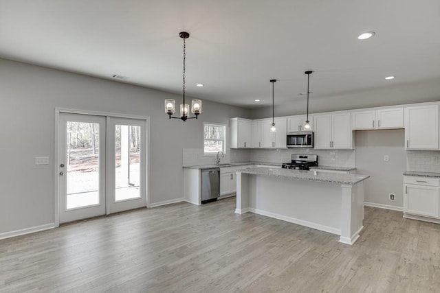 kitchen with sink, light stone counters, pendant lighting, white cabinets, and appliances with stainless steel finishes