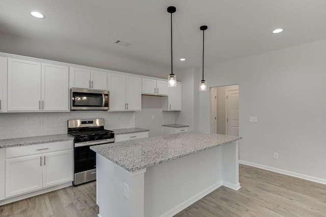 kitchen with white cabinets, appliances with stainless steel finishes, a center island, and light stone counters