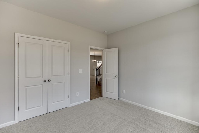 unfurnished bedroom with light carpet, a closet, and a chandelier