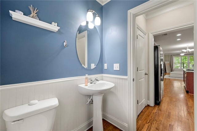 half bath with toilet, a sink, wood finished floors, and a wainscoted wall