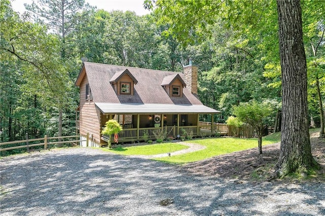 view of front of house with a chimney, gravel driveway, covered porch, fence, and a front lawn