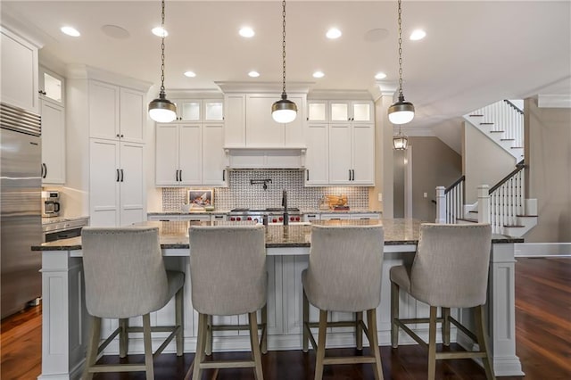 kitchen featuring dark wood-style floors, a kitchen island with sink, backsplash, and built in fridge