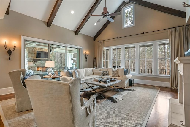 living area with ceiling fan, a lit fireplace, light wood finished floors, and beam ceiling