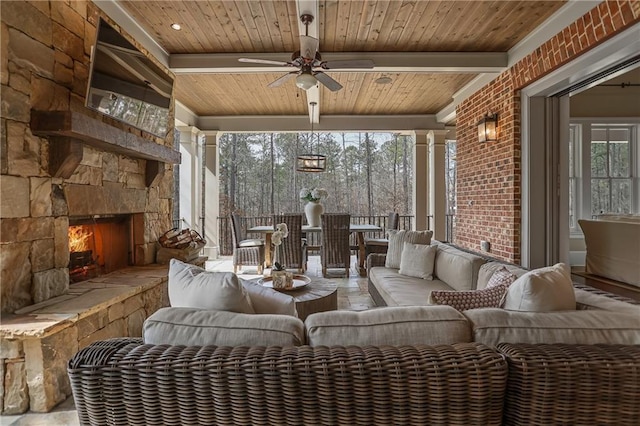 sunroom / solarium with ceiling fan, beamed ceiling, an outdoor stone fireplace, and wood ceiling