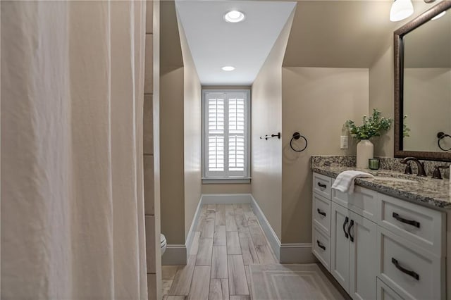 bathroom featuring baseboards, toilet, wood finished floors, vanity, and recessed lighting