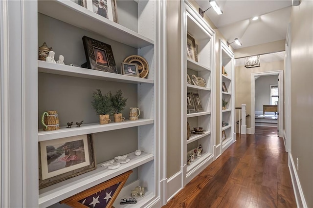 hall with built in shelves, dark wood finished floors, and baseboards