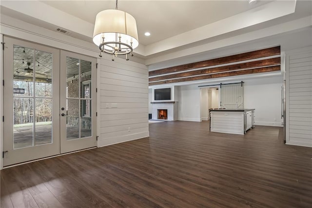 unfurnished dining area featuring visible vents, dark wood-style flooring, a lit fireplace, french doors, and a notable chandelier