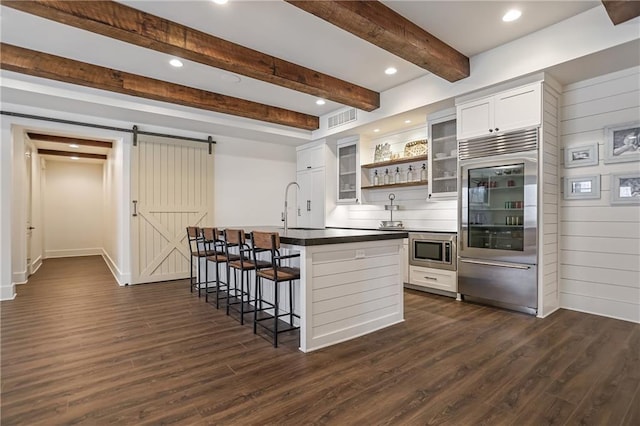 kitchen featuring a breakfast bar, dark countertops, visible vents, a barn door, and built in appliances