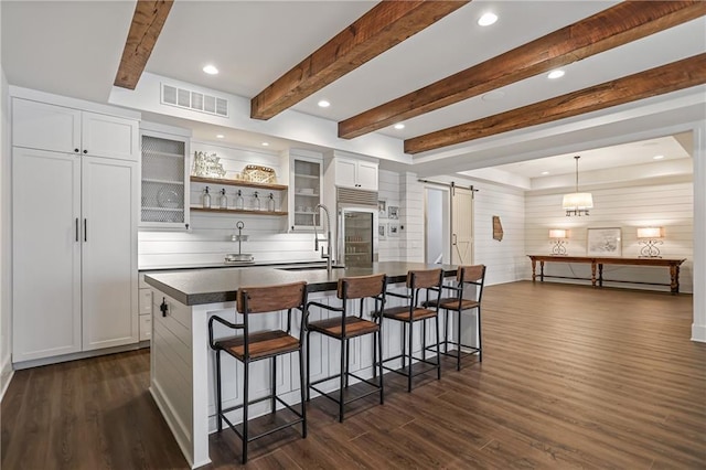 kitchen with a breakfast bar, visible vents, a barn door, a kitchen island with sink, and a sink