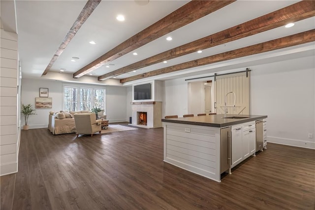 kitchen with a barn door, dark wood finished floors, dark countertops, open floor plan, and a sink