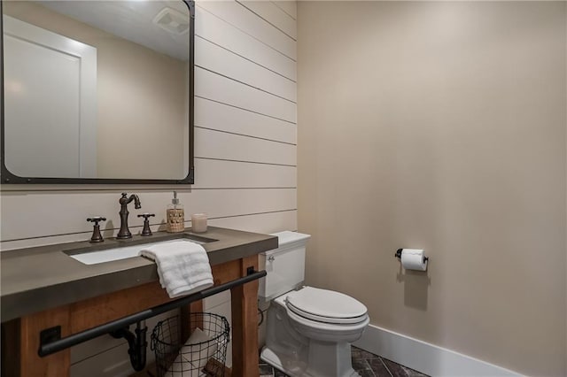 half bath with baseboards, a sink, visible vents, and toilet