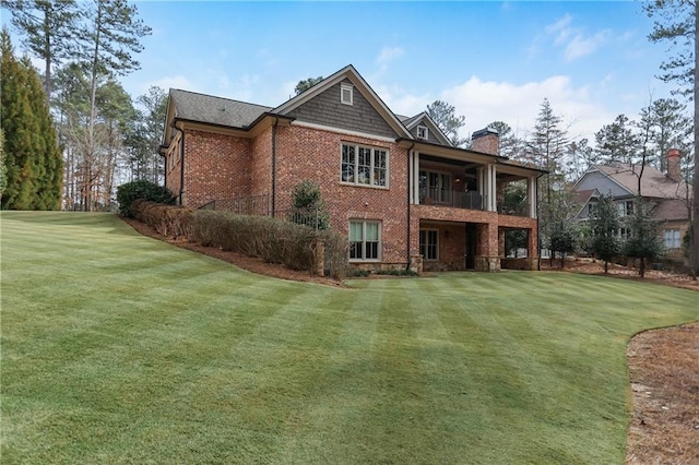 rear view of house featuring brick siding, a lawn, a chimney, and a balcony