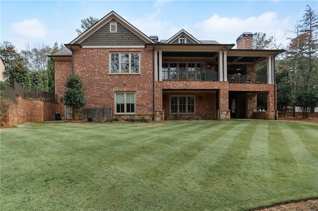 back of house with a balcony, brick siding, a chimney, and a yard