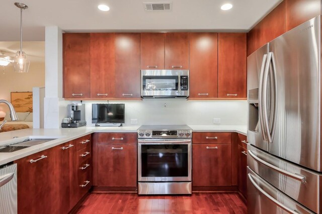 kitchen featuring dark wood-type flooring, stainless steel appliances, sink, and hanging light fixtures