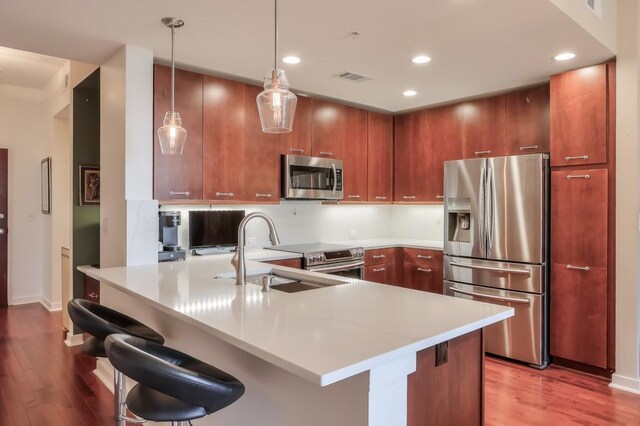 kitchen with decorative light fixtures, hardwood / wood-style floors, appliances with stainless steel finishes, kitchen peninsula, and sink