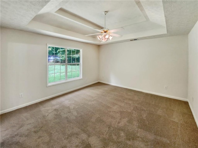 carpeted spare room featuring a raised ceiling, visible vents, ceiling fan, and baseboards