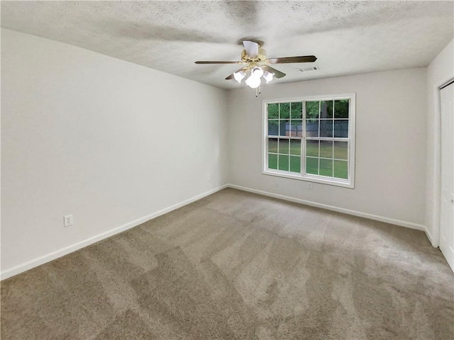 carpeted empty room featuring a textured ceiling, a ceiling fan, visible vents, and baseboards