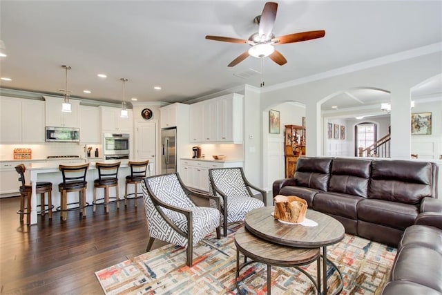 living room with crown molding, arched walkways, ceiling fan, and dark wood-type flooring