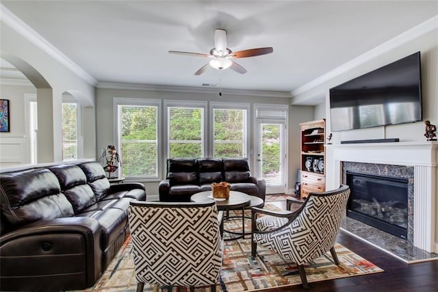living area featuring a healthy amount of sunlight, crown molding, a fireplace, and a ceiling fan