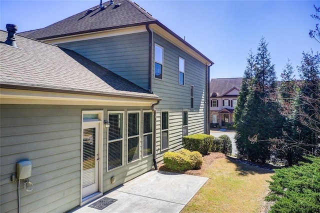 view of property exterior with a lawn, a shingled roof, and a patio area