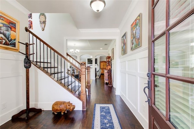 entryway with arched walkways, hardwood / wood-style flooring, a notable chandelier, ornamental molding, and stairs