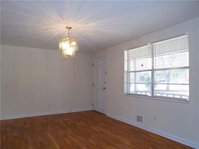 spare room with a notable chandelier and dark hardwood / wood-style floors