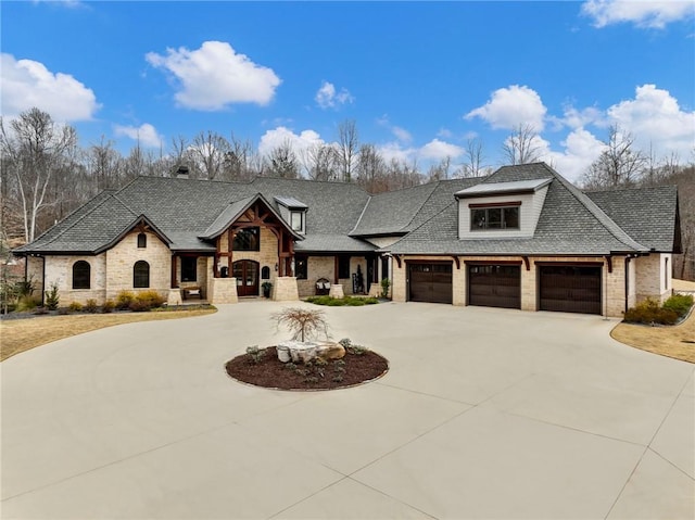 view of front of home with a garage, stone siding, curved driveway, and a shingled roof