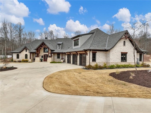 french provincial home featuring brick siding, a garage, driveway, and roof with shingles