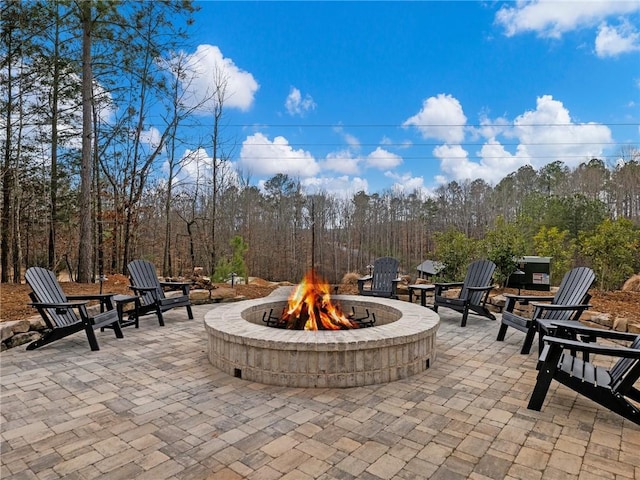 view of patio featuring an outdoor fire pit and a forest view