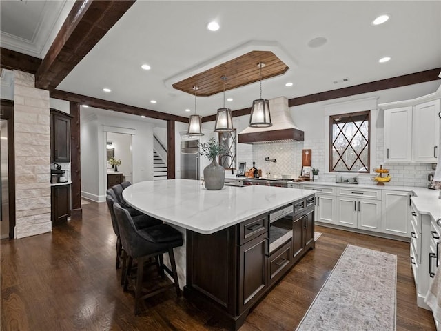 kitchen with stainless steel microwave, a center island, custom exhaust hood, white cabinets, and dark wood-style flooring