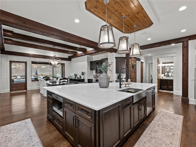 kitchen with a spacious island, a sink, light stone counters, appliances with stainless steel finishes, and dark wood-style flooring