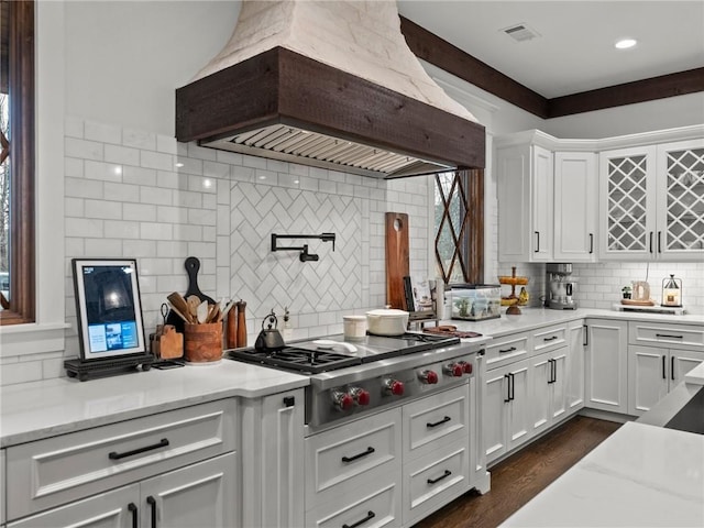 kitchen featuring visible vents, stainless steel gas cooktop, custom range hood, light stone counters, and white cabinets