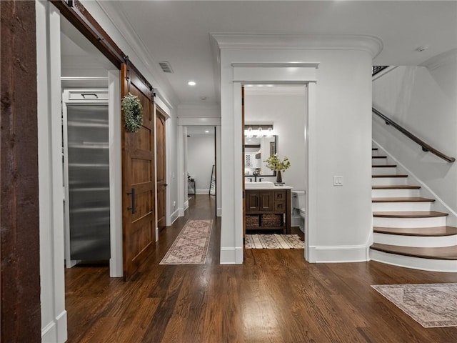 hallway featuring visible vents, stairway, a barn door, ornamental molding, and wood finished floors