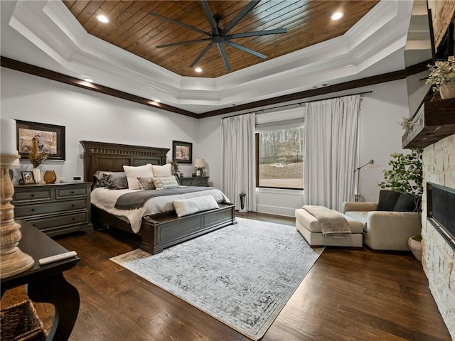 bedroom featuring a tray ceiling, a glass covered fireplace, dark wood-style floors, crown molding, and wood ceiling