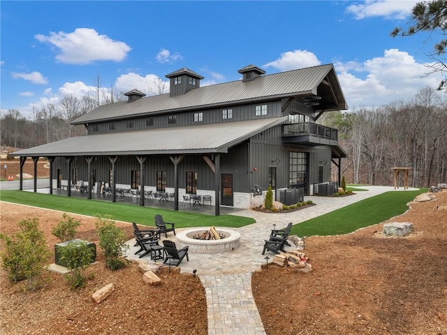 back of house featuring a balcony, a yard, a fire pit, a patio area, and metal roof