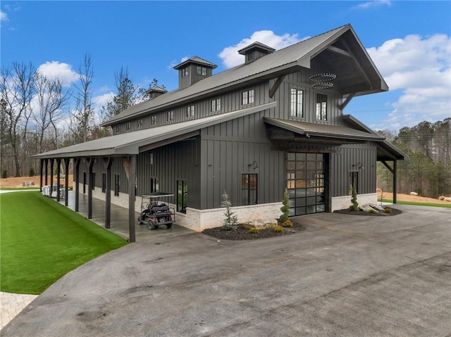 view of property exterior with a yard, board and batten siding, metal roof, and aphalt driveway