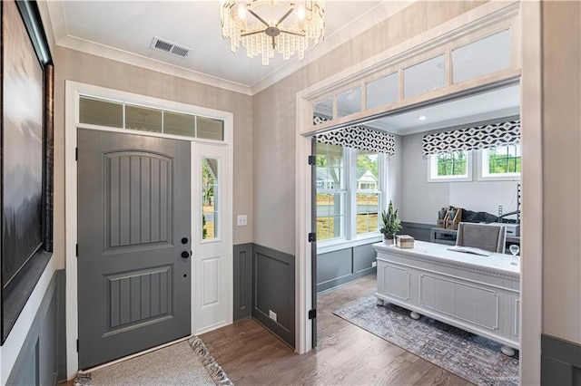 foyer entrance with wood-type flooring, crown molding, and an inviting chandelier